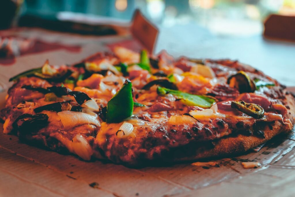 Close-up de uma pizza coberta com queijo derretido, pimentões verdes e cebolas sobre uma mesa de madeira Avenida General Flores em Colônia do Sacramento