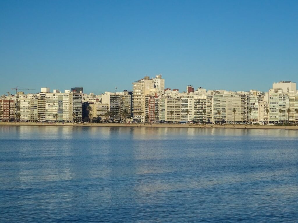 Skyline da orla de Pocitos em Montevideo, Uruguai, visto das águas do Rio da Prata. A imagem mostra a linha de edifícios residenciais modernos ao longo da Rambla, sob um céu azul limpo e águas calmas em primeiro plano.