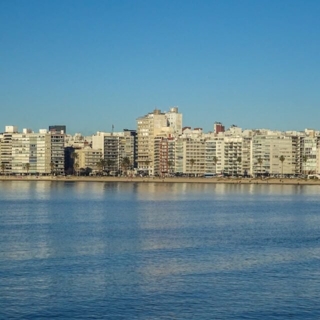 Skyline da orla de Pocitos em Montevideo, Uruguai, visto das águas do Rio da Prata. A imagem mostra a linha de edifícios residenciais modernos ao longo da Rambla, sob um céu azul limpo e águas calmas em primeiro plano.