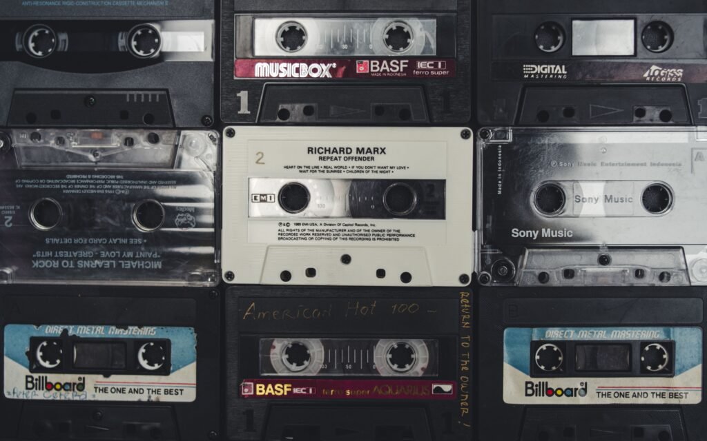 Imagem aproximada de uma grade de fitas cassete antigas, mostrando rótulos da Billboard, Sony Music, BASF e Musicbox, além de bobinas de fita visíveis Noite da Nostalgia no Uruguai