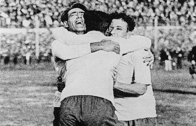 Abraço histórico entre os jogadores Alcides Ghiggia (autor do gol da vitória) e Obdulio Varela (capitão da seleção uruguaia), celebrando a vitória no Maracanazo em 1950. A foto em preto e branco retrata a emoção no campo logo após o fim da partida contra o Brasil no estádio do Maracanã.