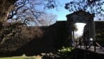 Vista da histórica Puerta de la Ciudadela (Portón de Campo) em Colonia del Sacramento, Uruguai. A imagem destaca o portão de pedra com arco, a ponte de madeira e as muralhas antigas que preservam o charme colonial do centro histórico, um dos destinos imperdíveis para turistas brasileiros.