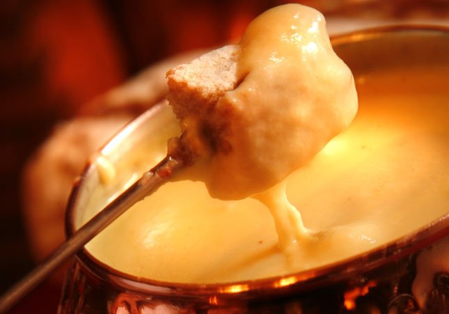 Bread dipped into a warm cheese fondue in a copper pot, held on a fork.
