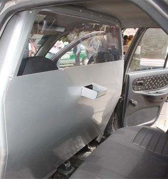 Open car door revealing a frosted privacy screen across the back seat area and a small white object attached to the screen; people are visible outside the car through the front window.