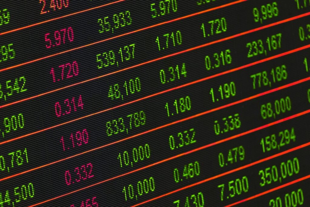 Stock market screen showing green and pink numbers with red trend lines across a dark background, indicating financial data.
