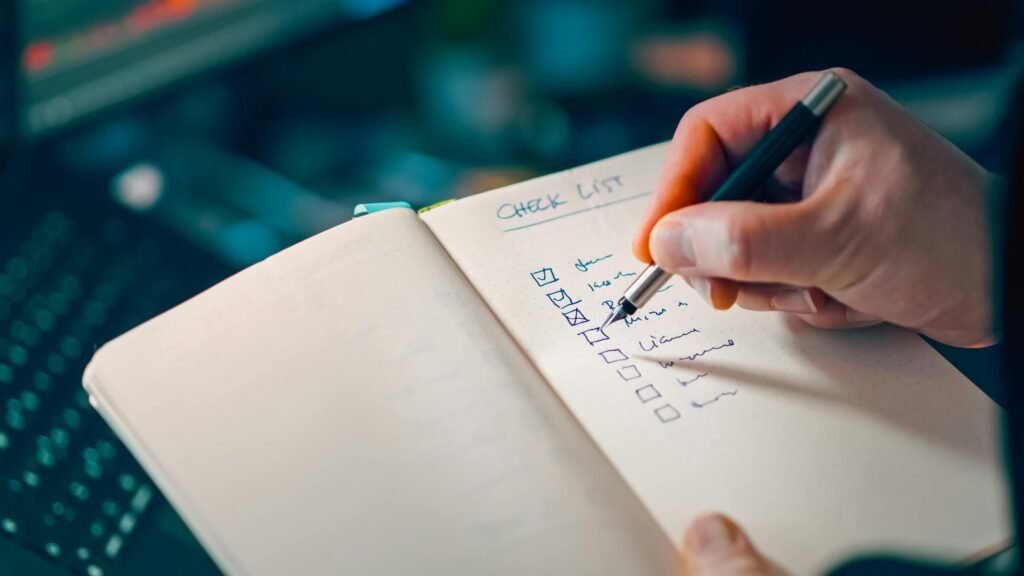 Close-up of a hand writing on a notebook page labeled 'CHECK LIST', filling in a to-do list with checkboxes