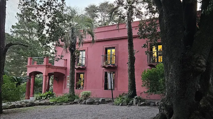 Casarão rosa histórico cercado de palmeiras e árvores no Arboretum Lussich