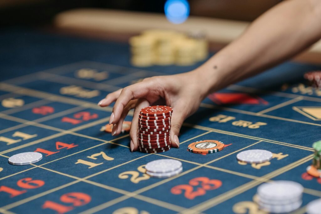 Uma mão empilha fichas vermelhas de cassino em uma mesa de roleta azul com casas de apostas numeradas à vista Cassino Carrasco em Montevideo