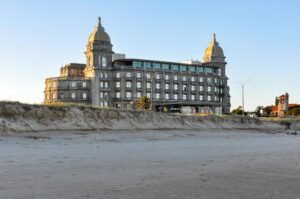 A imagem de um edifício histórico de pedra com duas torres em forma de cúpula, situado numa praia de areia e com um céu azul límpido ao pôr do sol, não está presente, mas o texto descreve bem a cena Cassino Carrasco em Montevideo