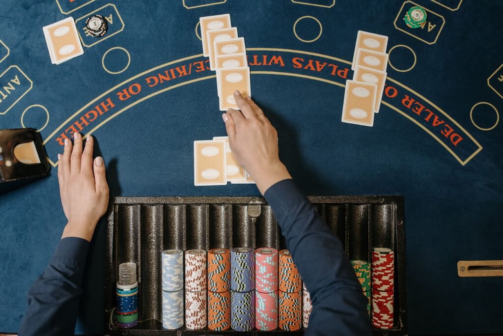 Vista aérea de uma mesa de pôquer de cassino com fichas coloridas empilhadas, cartas de baralho em jogo e mãos dos jogadores alcançando as cartas Cassino Victoria Plaza em Montevideo