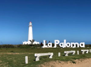 Farol de La Paloma branco ao lado do letreiro La Paloma sob céu azul