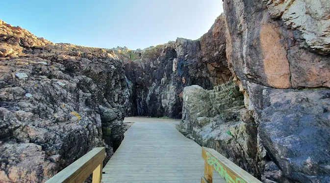 Passarela de madeira entre paredões rochosos no complexo de Las Grutas