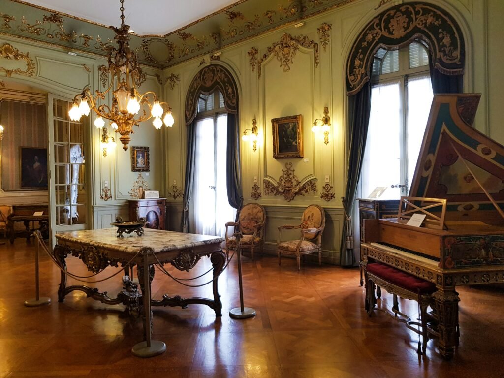 Sala de estar ornamentada do século XVIII com decorações douradas, lustre e piano.