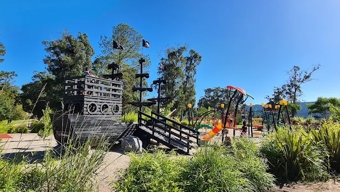 Playground com barco pirata de madeira cercado de vegetação no Parque El Jaguel