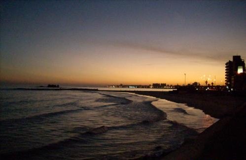 Pôr do sol na Praia de Malvín com as luzes da orla refletindo na água