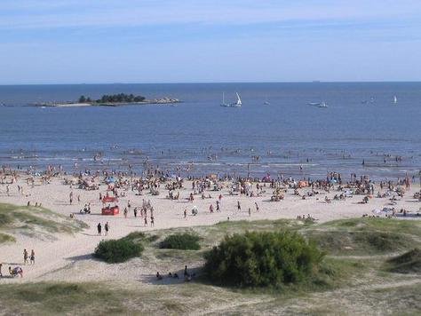 Praia de Malvín movimentada no verão com a Isla de las Gaviotas e veleiros ao fundo
