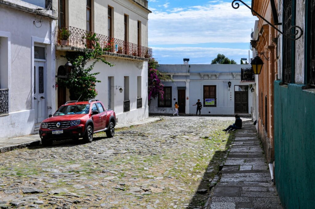 avenida em pedras, com diversas construções prediais e carro
