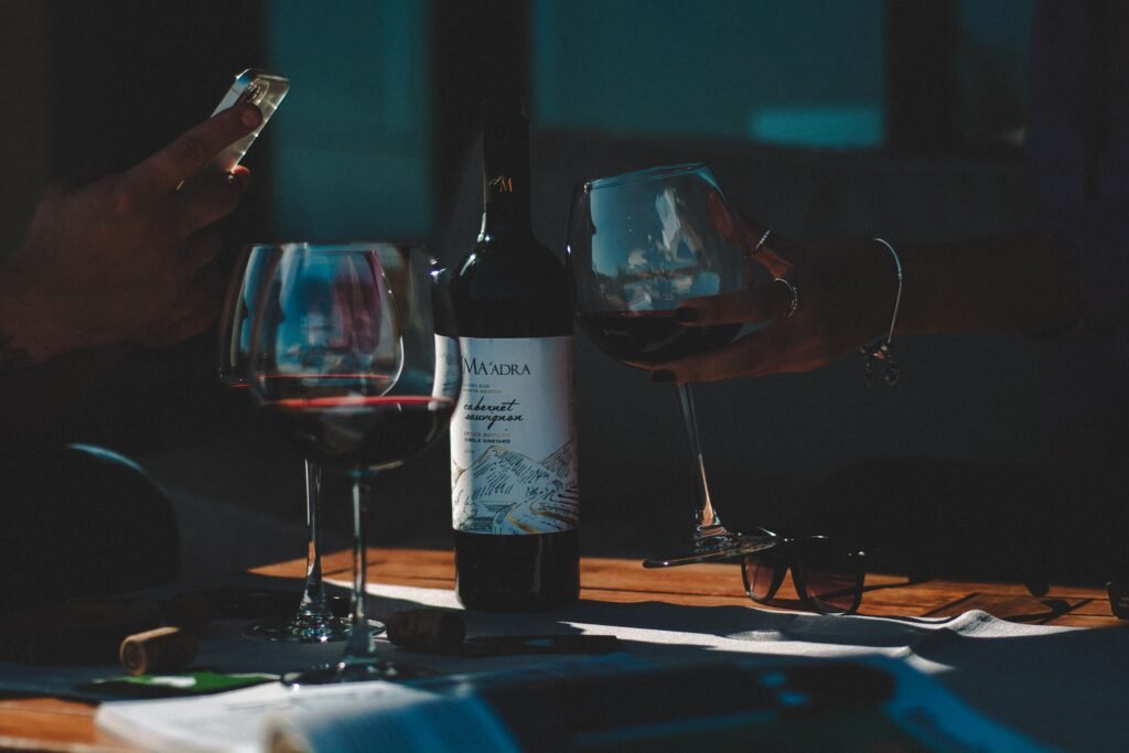 Garrafa de vinho entre duas taças sobre uma mesa de madeira em um ambiente intimista e com pouca luz.