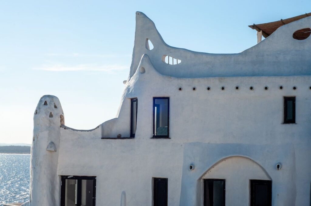 Detalhe da fachada branca e orgânica de Casapueblo com formas onduladas e janelas escuras voltadas para o mar