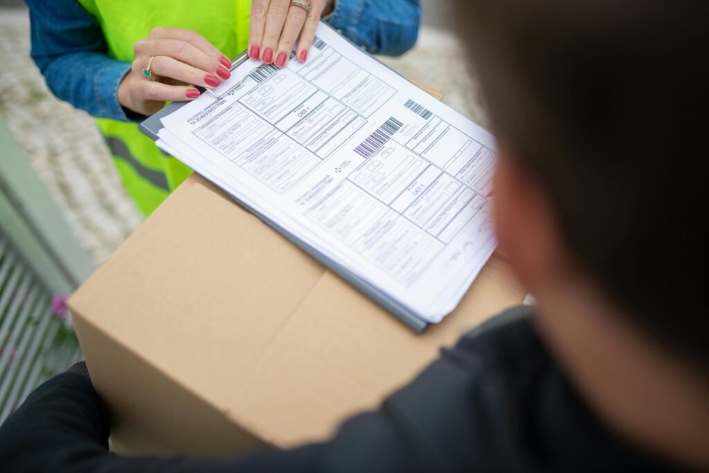 Uma pessoa vestindo um colete de segurança fluorescente segura formulários de remessa empilhados com códigos de barras sobre uma caixa de papelão ao ar livre correios no Uruguai