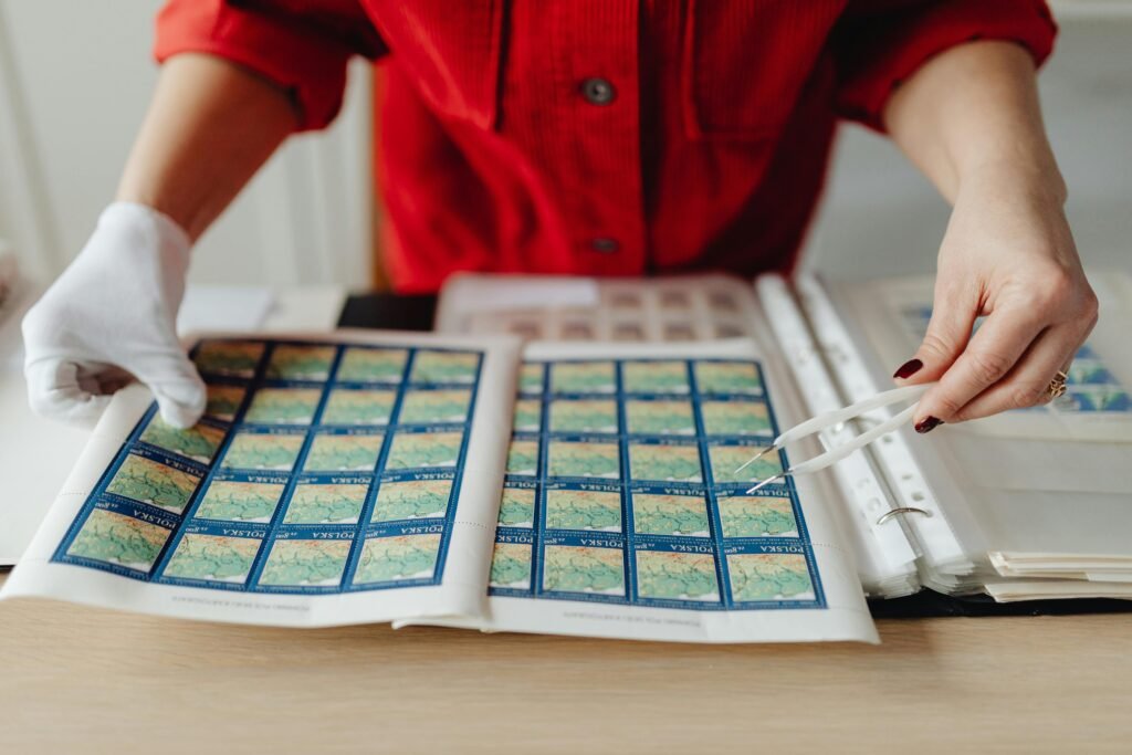 Close-up de uma pessoa com camisa vermelha e luvas brancas, separando selos azuis com tema de mapas em um álbum aberto correios no Uruguai