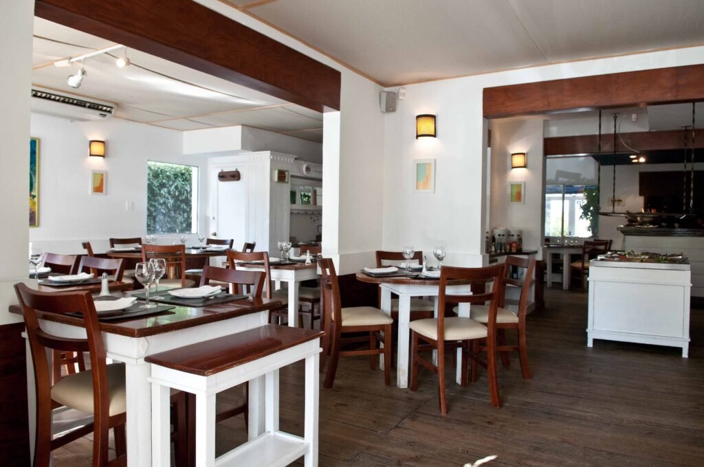 Salão interno do La Vaca Parrilla com mesas de madeira, cadeiras coloniais e parrilla à vista ao fundo