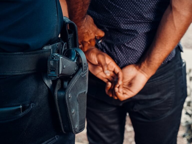 Police officer's sidearm secured in a holster on the belt beside a person standing with hands behind their back.