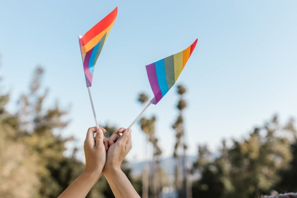 Mãos erguendo bandeiras com as cores do arco-íris contra o céu azul, simbolizando o Uruguai como destino gay friendly