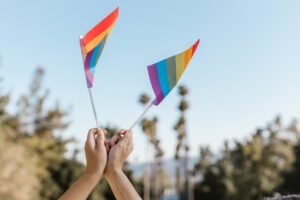 Mãos erguendo bandeiras com as cores do arco-íris contra o céu azul, simbolizando o Uruguai como destino gay friendly