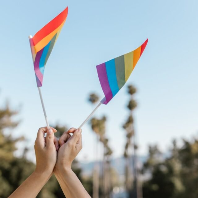 Mãos erguendo bandeiras com as cores do arco-íris contra o céu azul, simbolizando o Uruguai como destino gay friendly