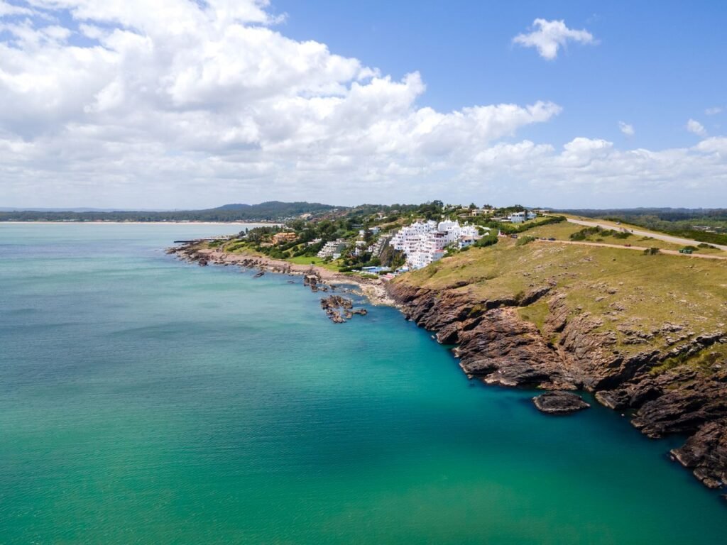 Vista aérea de Casapueblo sobre as falésias rochosas de Punta Ballena, com o mar esmeralda ao redor
