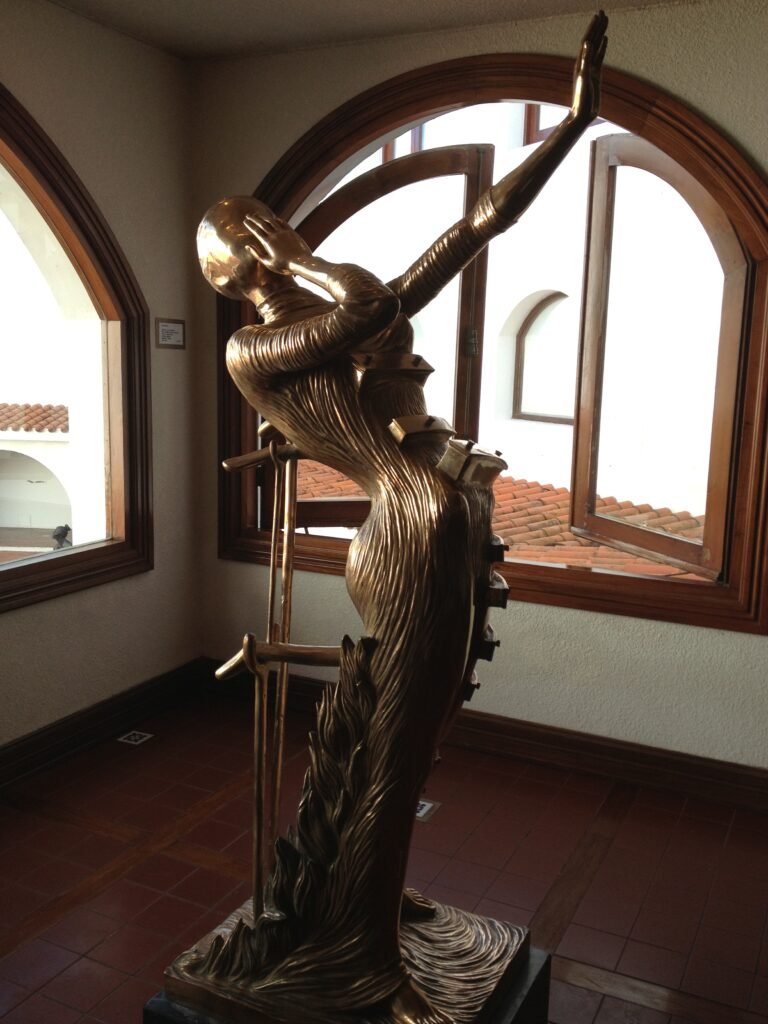Escultura em bronze dourado de figura feminina em movimento ascendente, exposta em galeria interna do Museo Ralli em Punta del Este.