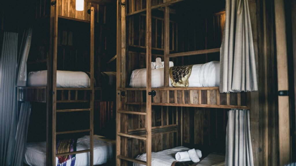 Quarto rústico com iluminação tênue, contendo beliches de madeira, roupa de cama branca e toalhas dobradas na cama de cima.