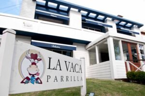 Exterior of La Vaca Parrilla restaurant: white building with blue awnings and a large sign featuring a cartoon bull logo.