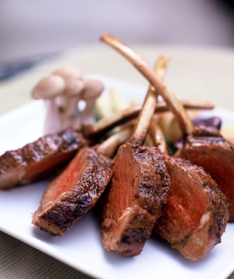 Costelas de cordeiro grelhadas ao ponto, servidas com cogumelos e legumes no restaurante La Vaca Parrilla