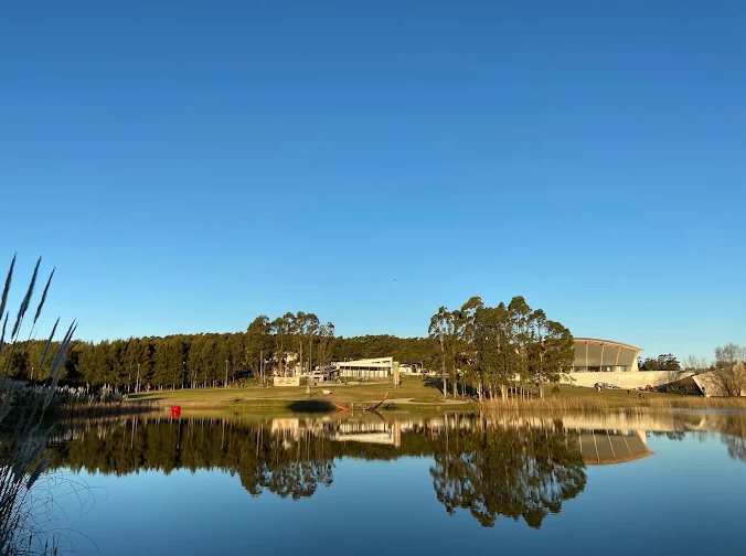 Lago espelhado refletindo árvores e o edifício da Fundación Pablo Atchugarry no Parque das Esculturas