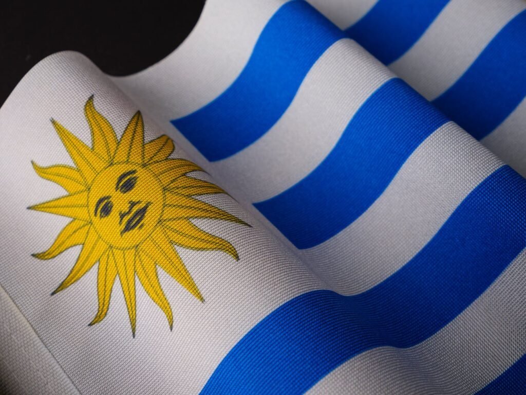 Bandeira do Uruguai com suas listras azuis e brancas e o Sol de Maio dourado em destaque