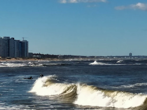 Surfistas no mar agitado da Praia El Emir com a orla de Punta del Este ao fundo