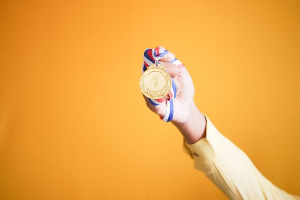 Mão erguendo uma medalha de ouro de primeiro lugar contra um fundo amarelo