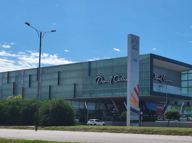 Fachada externa do Costa Urbana Shopping com a loja Daniel Cassin em dia ensolarado