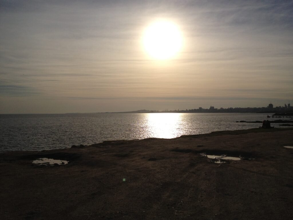 Sol refletindo sobre a água na Praia de Punta Carretas com a costa de Montevideo ao fundo