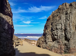 Passarela de madeira entre formações rochosas levando à praia em Las Grutas