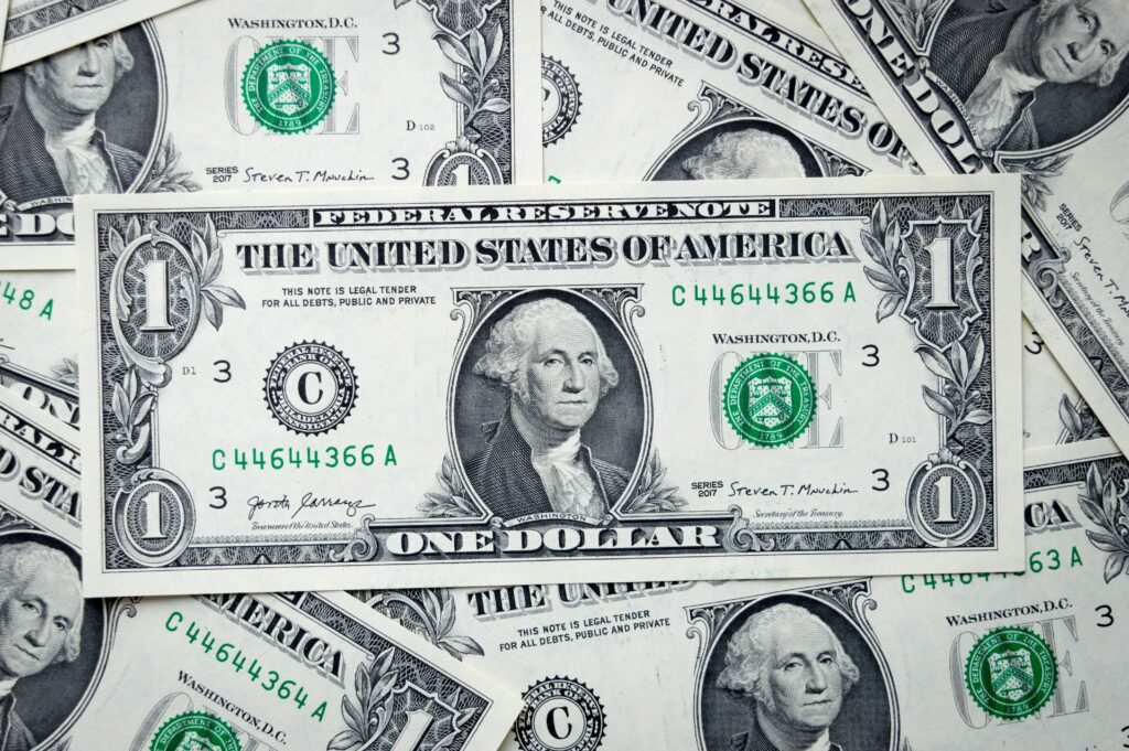 Notas de um dólar dos Estados Unidos espalhadas, apresentando o brasão de Washington e o selo verde do Tesouro.