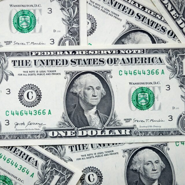 Notas de um dólar dos Estados Unidos espalhadas, apresentando o brasão de Washington e o selo verde do Tesouro.