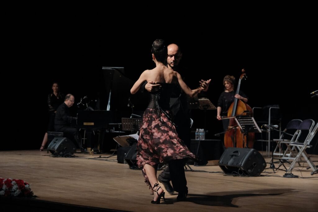 casal dançando tango num palco, com músicos ao fundo