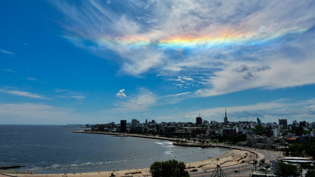 vista litorânea, com o céu azul, um arco-íris e a cidade