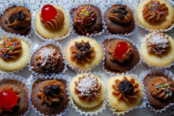 Cupcakes variados com massa de chocolate e baunilha, decorados com confeitos, cerejas e flocos de coco, dispostos em uma bandeja.