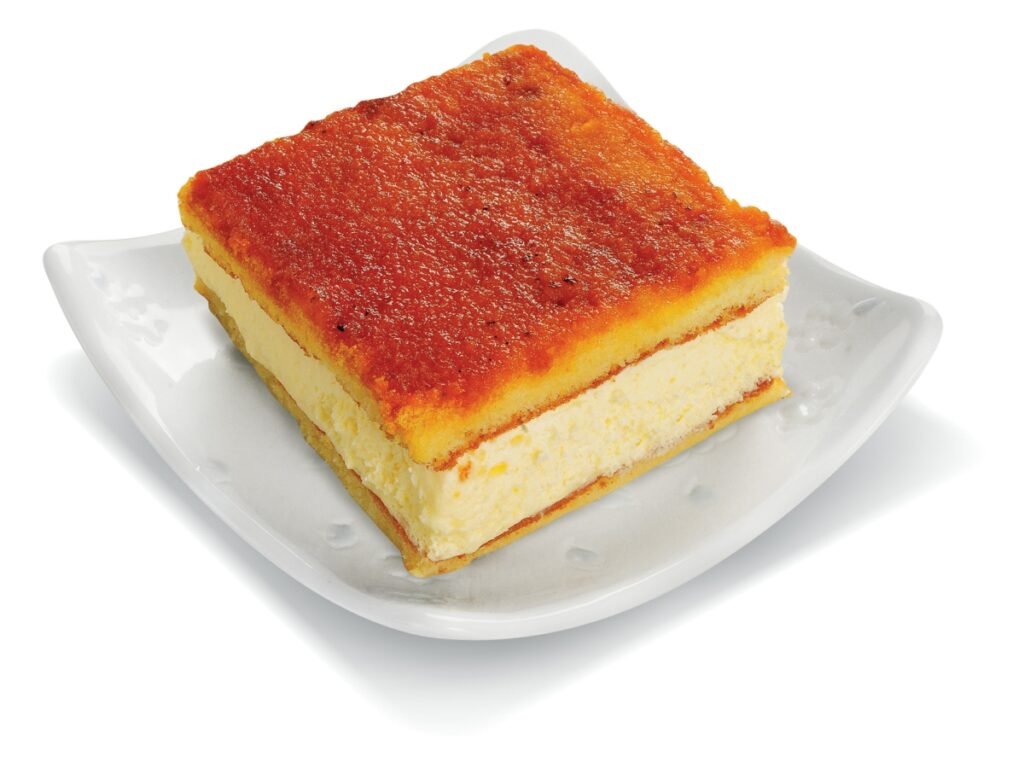 Fatia de cheesecake com o topo dourado e caramelizado em um prato branco.