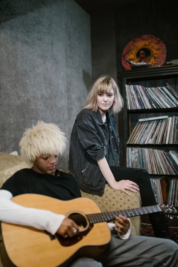 Dois músicos com violão numa sala cercada de discos