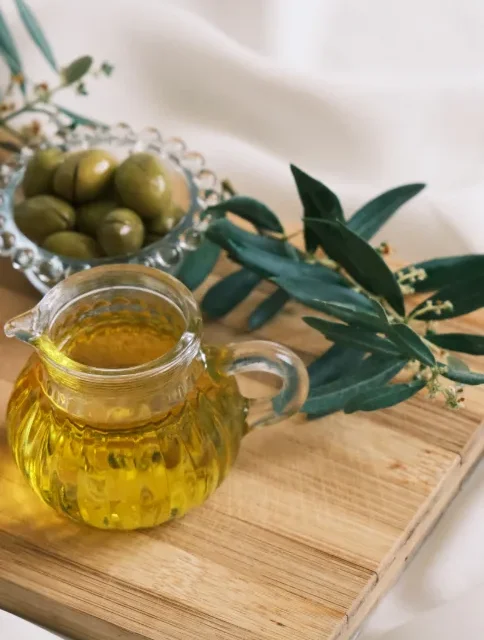 Jarra de vidro com azeite de oliva ao lado de azeitonas e ramos